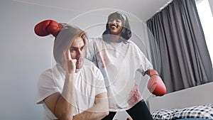 Young woman distracting her boyfriend from working on laptop. Attention seeker with boxing gloves playing with partners