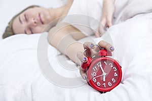 Young woman do not want to wake up and hand putting the alarm clock.