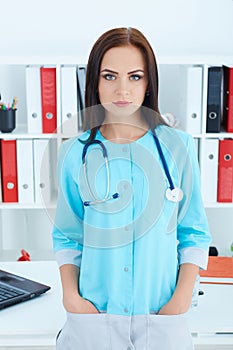 Young woman doctor with blue coat standing in hospital. Medical help or insurance concept.