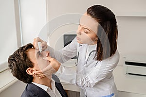 Young woman doctor eye specialist drip drops in patient eye