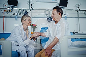 Young woman doctor holding hand, and talking with her patient.