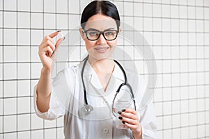 Young woman doctor holding and showing one white natural pill