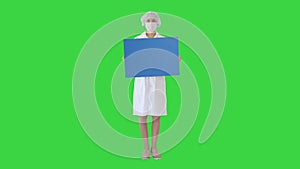 Young woman doctor in a mask holding an empty bill board on a Green Screen, Chroma Key.