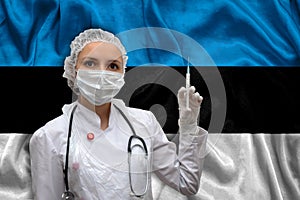 Young woman doctor in medical uniform on the background of the national flag of Estonia is holding a syringe. The concept of a new