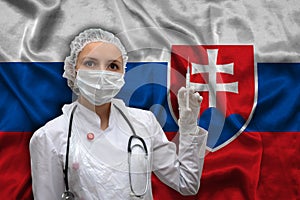 Mladá lekárka v lekárskej uniforme na pozadí štátnej vlajky Slovenska drží injekčnú striekačku. Pojem