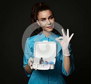 Young woman doctor nurse in blue uniform and protective latex gloves holding first aid kit in hands gesturing