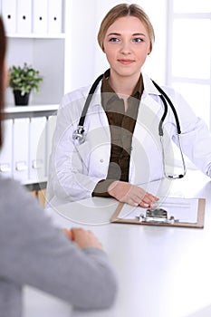 Young woman doctor and patient at medical examination in hospital office. Khaki colored blouse of therapist looks good