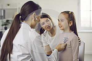 Young woman doctor pediatrician in medical uniform examining little smiling girl with stethoscope