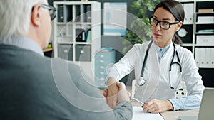 Young woman doctor shaking hands with elderly man patient talking in office