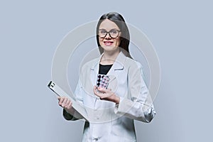 Young woman doctor showing medicine pills on gray background