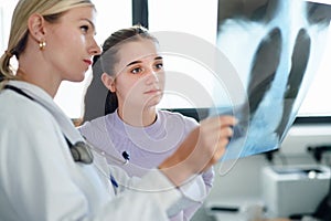 Young woman doctor showing x-ray image of lungs to her patient.