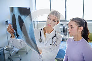 Young woman doctor showing x-ray image of lungs to her patient.