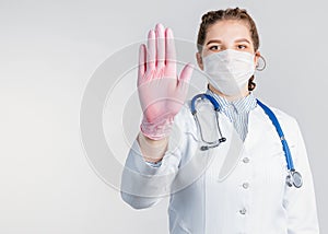 Young woman doctor shows stop gesture on white background. Say No virus disease. Copy space