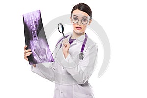 Young woman doctor with stethoscope looking at x-ray thinking about diagnosis in white uniform on white background