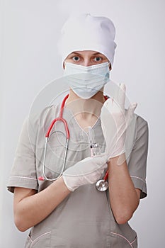 young woman doctor with stethoscope in mask putting on gloves on white background in clinic hospital. individual protection means