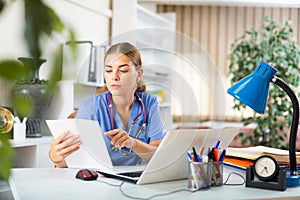 Young woman doctor studies the patient's outpatient card while sitting at a computer in the office