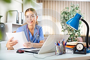 Young woman doctor studies the patient's outpatient card while sitting at a computer in the office