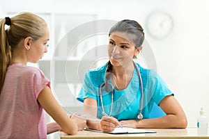 Young woman doctor talking to her teenager patient and writing down the symptoms. Concept of visit to gynecologist