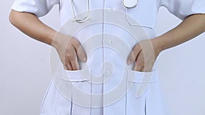 Young woman doctor in white coat with her hands in pockets on a white background.