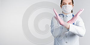 Young woman doctor in a white coat and pink sterile gloves shows a stop gesture on white background. Copy space