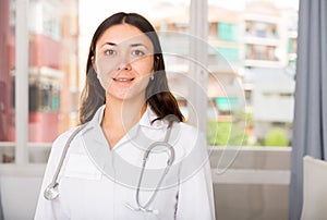 Young woman doctor in white uniform standing in clinic`s office