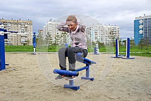 A young woman does exercises for abdominals on the street on simulators