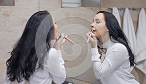 A young woman does daily face care before going to work, paints her lips with lipstick. Brunette in the bathroom getting ready for