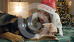 Young woman and dog in glasses are resting on the bed at home. Love, togetherness and pets. woman is reading a book