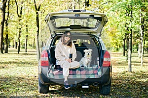 Young woman with a dog relaxing and enjoying nature sitting in car trunk