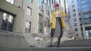 Young woman with the dog is standing in the foreground of building