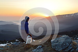 Young woman and dog at sunrise high in the mountain