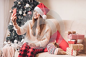 Young Woman and dog in sweater takes selfie portrait on the smartphone at winter holidays, enjoy Christmas time at home