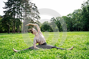Young woman doing aerobics, pilates, yoga or stretching on green grass in park