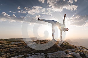 Young woman doing beautiful yoga, sunset or sunrise in mountains over blue sky and clouds against sunlight. Healthy