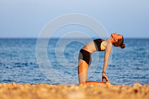 Young woman doing camel pose on her yoga routine at the beach