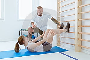 Young woman doing crunches on the gym floor, a helpful trainer motivating her