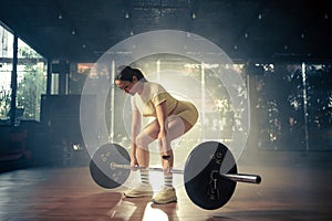 Young woman doing deadlift with heavy bar in gym, strong female athlete with muscular body lifting weights, exercising with