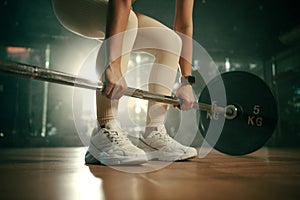 Young woman doing deadlift with heavy bar in gym, strong female athlete with muscular body lifting weights, exercising with