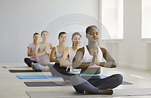 Young woman doing easy asanas, breathing exercises and meditating during group yoga.