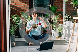 Young woman doing exercise yoga, playing on tibetan singing bowl with its mallet in cozy modern loft style room full of