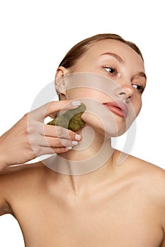 Young woman doing facial massage with guasha scrapper. Concept of beauty, skin care, self-massage, spa procedure at home