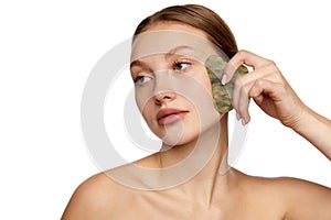 Young woman doing facial massage with guasha scrapper. Concept of beauty, skin care, self-massage, spa procedure at home