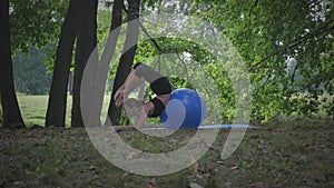 A young woman is doing gymnastic exercises in a summer park in a tracksuit. Healthy lifestyle.