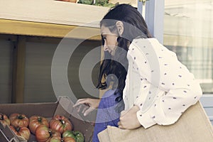 Young woman doing healthy shopping, buying tomatoes in a greengrocer outdoors with eco duffle bag