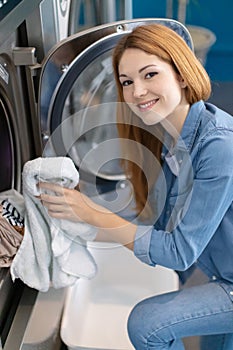 young woman doing weekly washing in laundromat