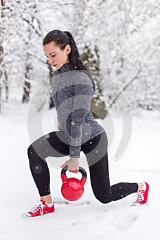 Young woman doing lunge exercise with kettlebell in snow