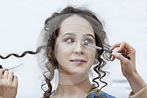 A young woman is doing make-up. Bright brunette with curly hair. Beauty industry. Close-up. Light background