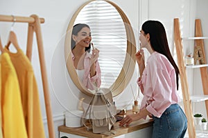 Young woman doing makeup near mirror at home. Morning routine