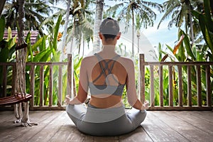 Young woman doing meditation in wooden porch in vacation summer resort. Rear view of young female meditating outdoors.