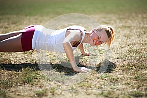 Young woman doing push ups exercise, workout on grass